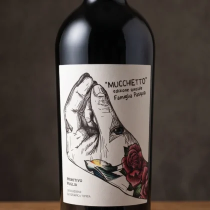 Butelka ukazująca czerwone wino primitivo Mucchietto Puglia IGT, obok kieliszka wypełnionego rubinowym trunkiem.